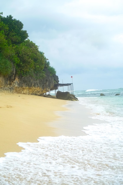 Foto uma praia com um pontão rochoso e um pequeno barco na água.