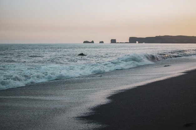 Uma praia com uma praia de areia preta e uma grande formação rochosa ao fundo.