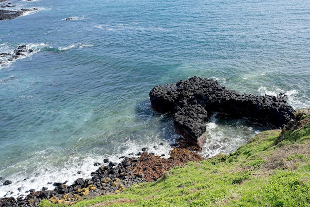 Uma praia rochosa com uma praia de areia preta e uma colina coberta de grama verde.