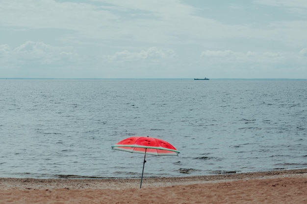 Uma praia vazia Um guarda-sol do sol na margem de um rio ou do mar Guarda-chuva em forma de melancia Um navio no horizonte