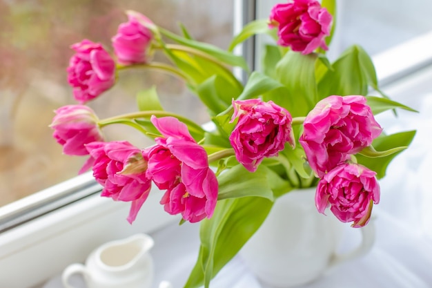 Uma primavera ainda vida um buquê de tulipas em um vaso uma xícara de chá e um livro velho estão deitados na janela