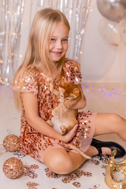 Uma princesinha em um vestido elegante segura um gatinho vermelho nas mãos. O símbolo do ano