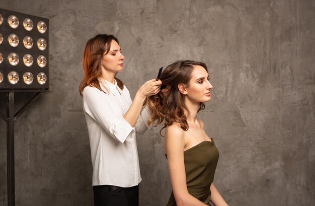 Uma profissional mulher faz um penteado para o cabelo de uma modelo em um fundo cinza com um lugar para texto