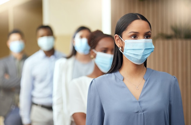 É uma questão de saúde e segurança Foto recortada de uma jovem empresária atraente usando uma máscara no início de uma fila em seu escritório