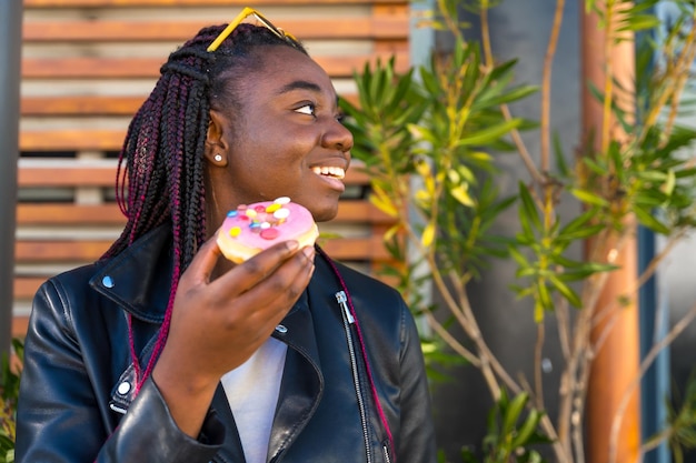 Uma rapariga africana distraída a comer donuts ao ar livre.