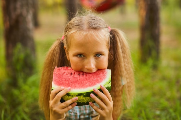 Uma rapariga bonita a comer melancia no parque da floresta.