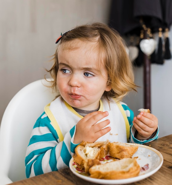 Foto uma rapariga bonita a comer pão à mesa em casa.