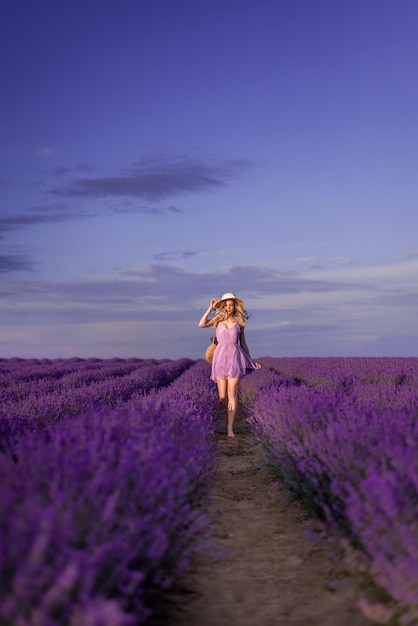 Foto uma rapariga com um chapéu e um vestido lila corre para um campo de lavanda.