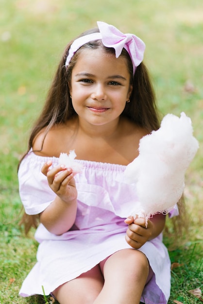 Uma rapariga engraçada de vestido rosa come algodão doce no verão no parque.