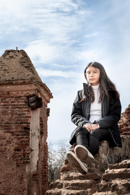 Foto uma rapariga está sentada numa parede em frente a um edifício antigo.