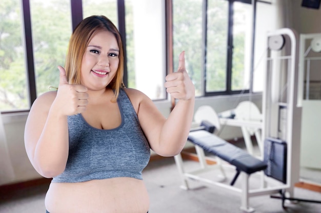 Uma rapariga gorda a mostrar o polegar no ginásio.