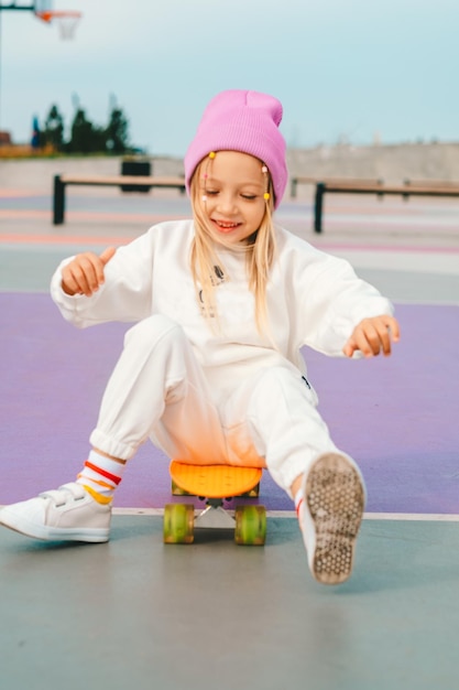 Foto uma rapariga loira anda de skate. uma rapariga elegante ri-se e vai de skate.