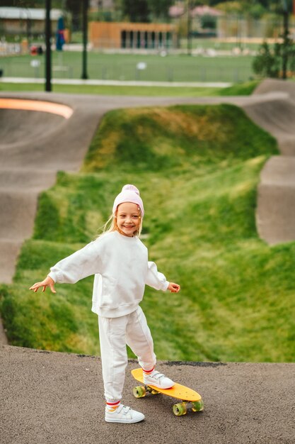 Foto uma rapariga loira anda de skate. uma rapariga elegante ri-se e vai de skate.