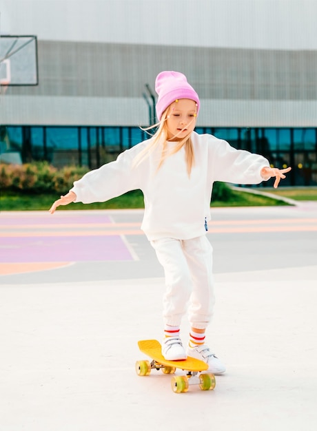 Foto uma rapariga loira anda de skate. uma rapariga elegante ri-se e vai de skate.