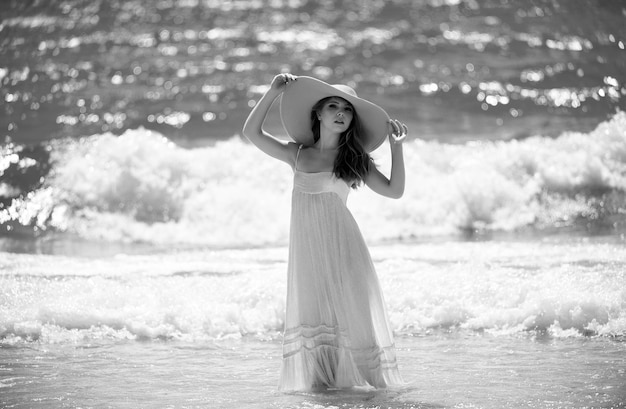 Uma rapariga sensual com um chapéu de palha a desfrutar de um banho de sol na praia. Uma mulher sexy e bronzeada a disfrutar da brisa à beira-mar.