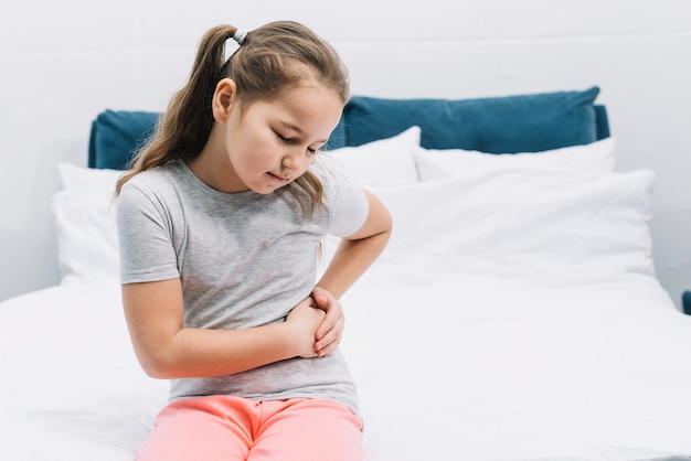 Uma rapariga sentada na cama com dores abdominais.