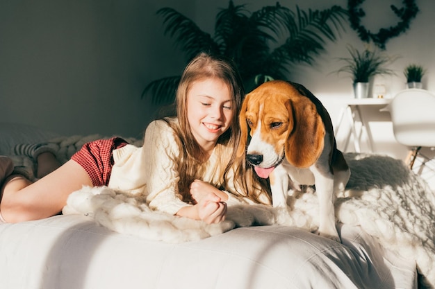 Uma rapariga sorridente com um cão a relaxar na cama em casa.