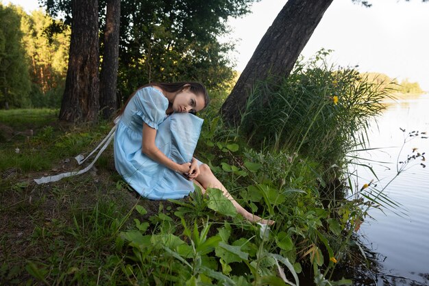 Uma rapariga triste com um vestido azul pensa em suicídio junto ao lago.