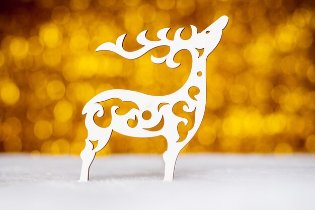 Uma rena branca decorativa cortada em madeira compensada em um fundo bokeh dourado desfocado a rena é um símbolo do Natal e do Ano Novo