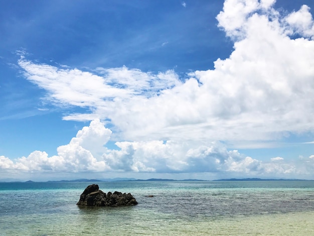 Uma rocha solitária no mar com nuvens no fundo do céu azul em um dia ensolarado