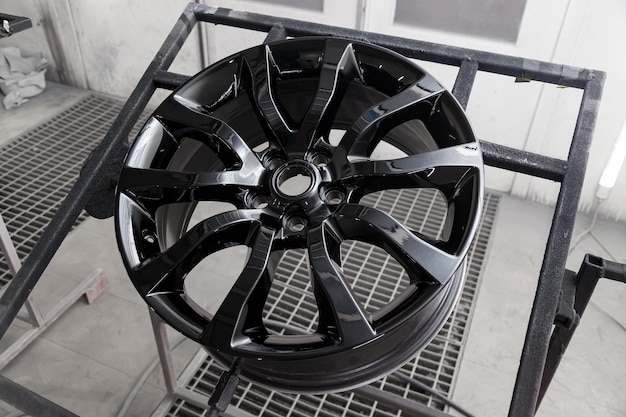 Foto uma roda de liga de alumínio pintada de preto é montada em uma estrutura especial durante a secagem em uma câmara em uma oficina de reparação de carrocerias indústria de serviços automotivos