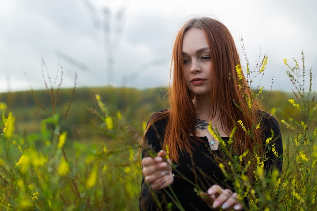 Uma ruiva pensativa, com um rosto triste, fica entre as flores silvestres