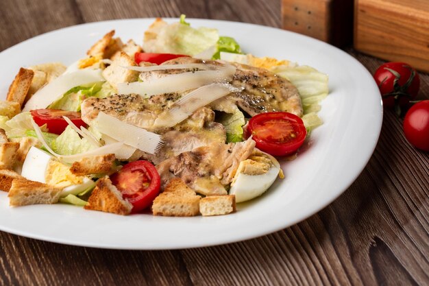 Uma salada Caesar com peitos de frango grelhados croutons de alface ovos tomate cereja vestido com queijo parmesão e molho sobre fundo de madeira