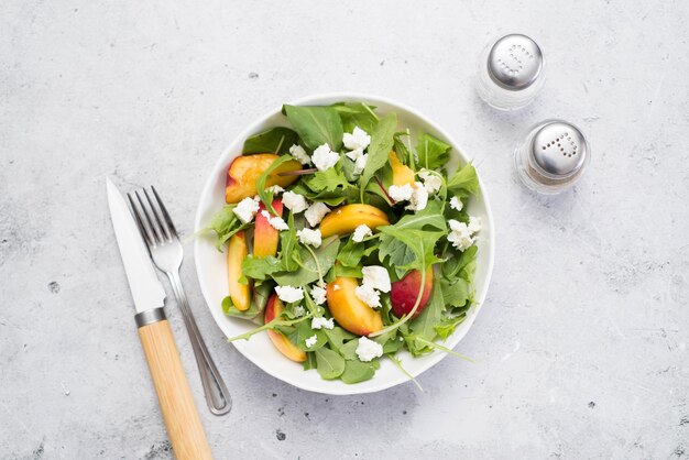 Uma salada leve de verão de pêssegos rucolla e colher e faca de queijo sobre fundo cinza claro