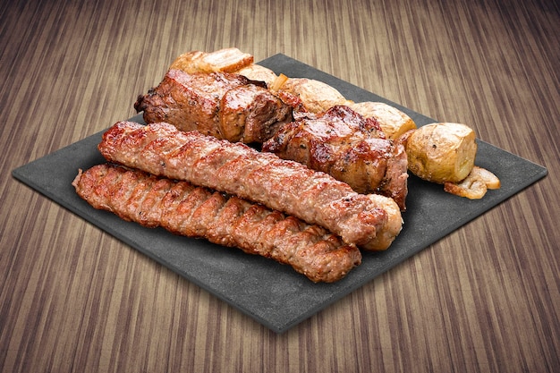 Uma seleção de várias carnes gourmet grelhadas em uma placa preta com um fundo rústico de madeira Pork kebab lyulya batatas