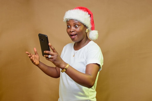 Uma senhora africana feliz olhando para o smartphone em sua mão e também com um boné de Natal na cabeça