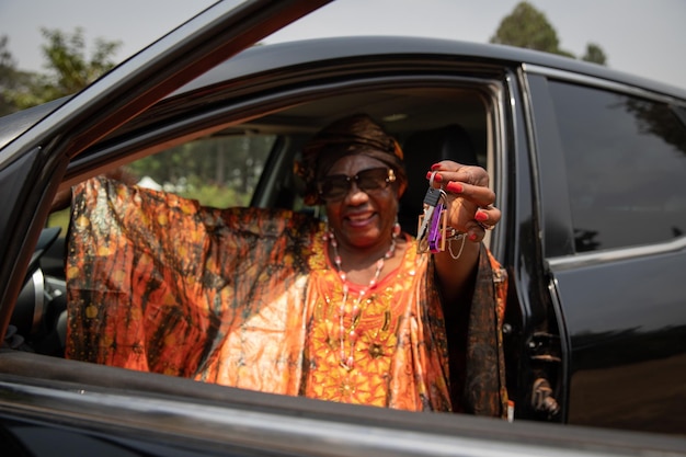 Uma senhora africana sentada em seu carro segura as chaves em seu conceito de serviços de aluguel de carros de mão