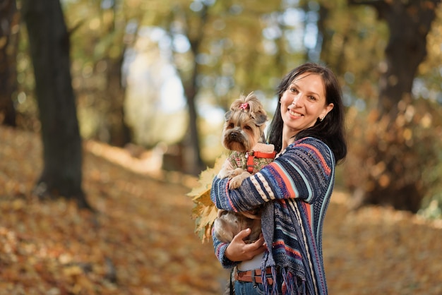 Uma senhora caminha no parque com um cachorrinho em um clima ensolarado