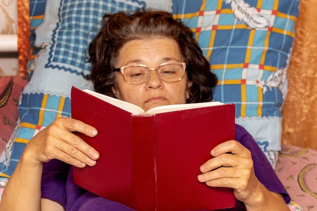 Uma senhora idosa está deitada na cama lendo a Bíblia
