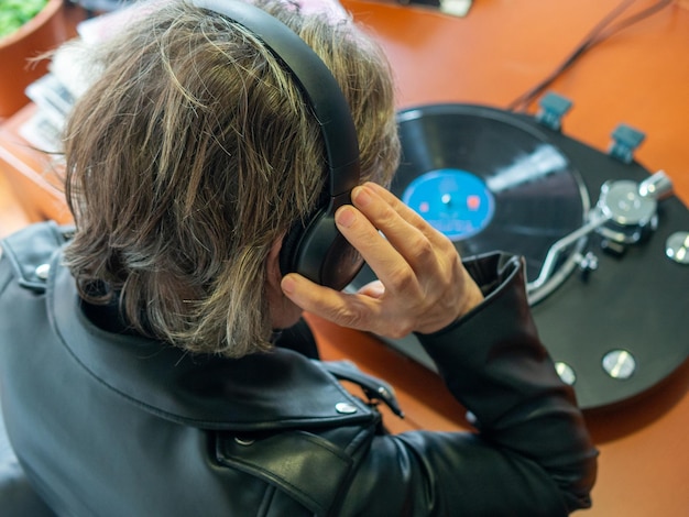 Foto uma senhora irreconhecível colocando seus fones de ouvido enquanto sua toca-discos está tocando um disco de vinil