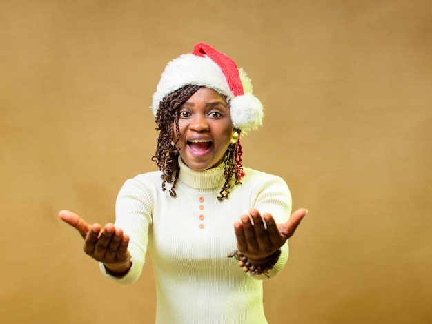 Foto uma senhora ou mulher africana fofa fazendo um gesto acenando em direção à câmera e também com um boné de natal na cabeça