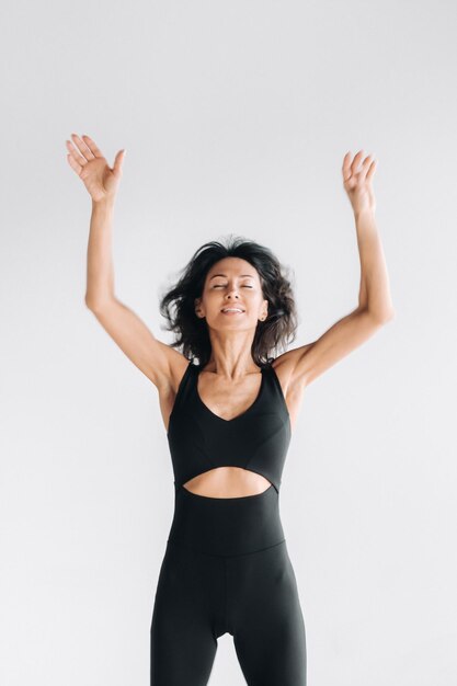 Uma silhueta embaçada de uma mulher em roupas esportivas pretas salta e levanta os braços contra um fundo branco
