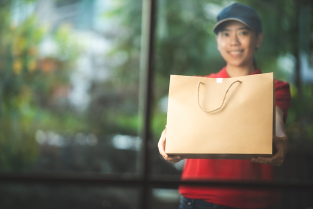 Uma sorridente jovem mulher asiática entrega mercadorias na frente da porta da casa, conceito de varejo online, entrega rápida, conceito de estilo de vida urbano, serviço de compras online, transporte.