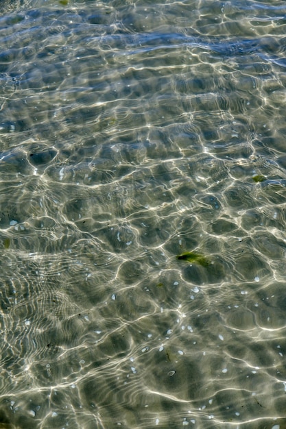 Uma superfície de água clara na costa do mar com a concha e água ondulada em um dia ensolarado A vista superior da água do mar transparente à beira-mar com o reflexo da luz do sol espalhada sob a água