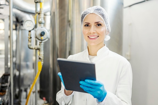 Uma supervisora de fábrica de leite usando tablet e sorrindo para a câmera