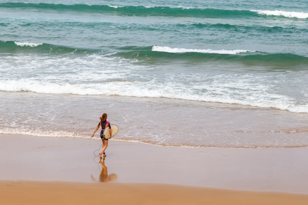 Uma surfista na praia entrando no oceano com sua prancha