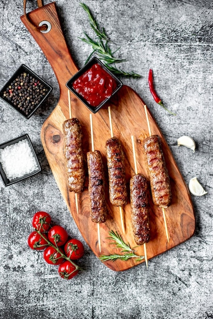 Foto uma tábua de corte de madeira com salsichas grelhadas e uma pequena tigela de molho vermelho.