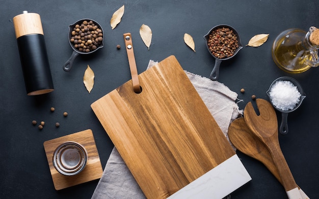 Foto uma tábua de corte de madeira vazia, sal, pimenta e azeite de oliva em uma garrafa em uma mesa preta