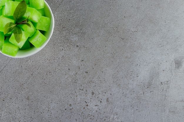 Uma tigela branca cheia de doces verdes doces com folhas de hortelã em uma mesa de pedra.