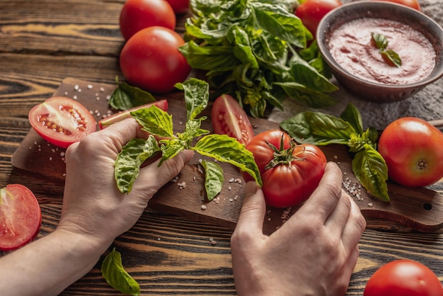 Uma tigela com molho italiano tradicional fresco e mãos segurando um tomate caseiro maduro e manjericão perfumado