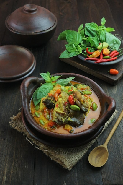 Uma tigela de comida tailandesa com uma colher e uma tigela de legumes em uma mesa de madeira.