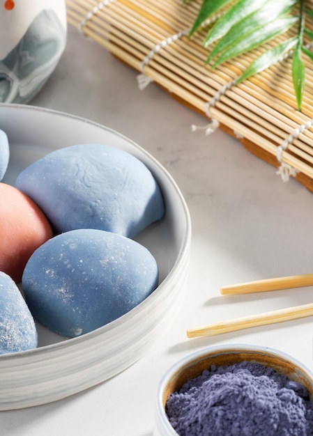 Uma tigela de mochi japonês com pauzinhos e tapete de madeira na bancada branca Conceito de uma sobremesa tradicional japonesa na mesa da cozinha Bolo de arroz asiático sorvete mochi Comida de rua doce asiática