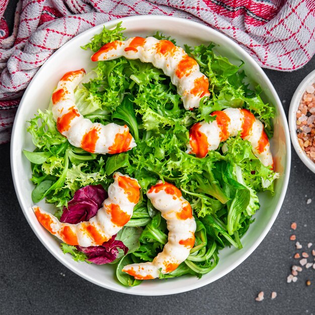 Uma tigela de salada com camarões e alface por cima.