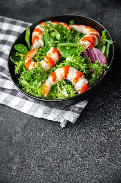 Uma tigela de salada com camarões e verduras em um fundo preto.