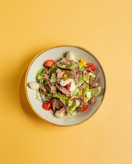 Uma tigela de salada de carne com legumes em um fundo amarelo