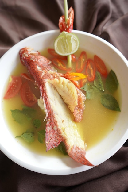 Uma tigela de sopa de peixe com uma rodela de limão por cima